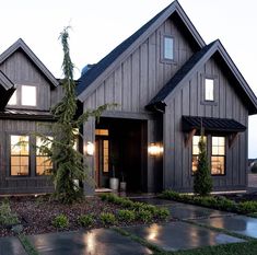 a house that is made out of wood and has windows on each side, along with plants in the front yard