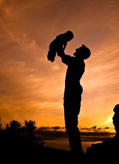 the silhouette of a man holding a child up to his face as the sun sets