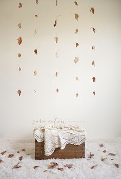 a blanket on top of a wooden box in front of a wall with falling leaves