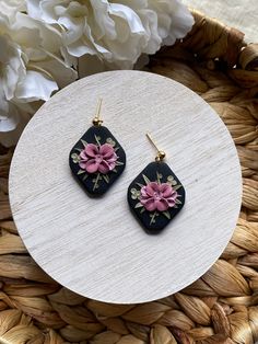 two square shaped earrings with pink flowers on them sitting on top of a wooden table