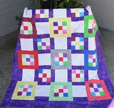 a purple and green quilt sitting on top of a cement ground next to a potted plant