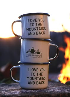 two coffee mugs sitting next to each other on top of a wooden table in front of a fire