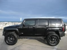 a black jeep parked on top of a parking lot next to the ocean and rocks