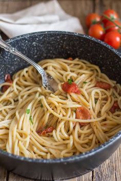 a bowl filled with pasta and tomatoes on top of a wooden table next to a fork