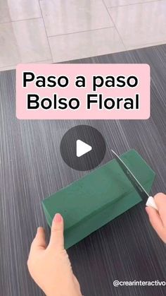 a person cutting paper with scissors on top of a wooden table in front of a sign that says paso a paso bolso floral