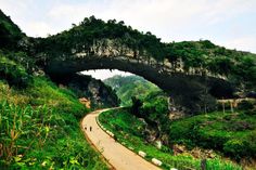 an arch bridge over a dirt road in the middle of a lush green mountain range