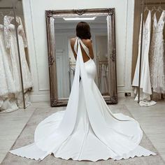 a woman in a wedding dress looking at herself in the mirror with her back to the camera