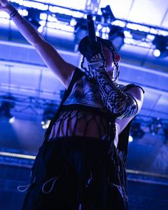 a woman with her arms in the air while wearing a mask and holding a microphone