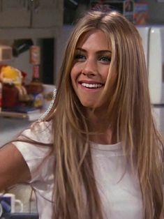 a woman with long blonde hair standing in front of a counter and smiling at the camera