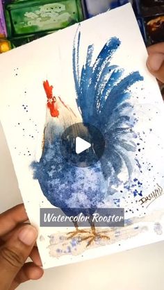 a person holding up a card with a blue rooster on it's back and the words watercolor rooster written in red