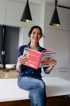 a woman sitting on a kitchen counter reading a book