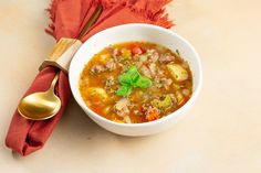 a white bowl filled with soup next to a spoon and red napkin on top of a table