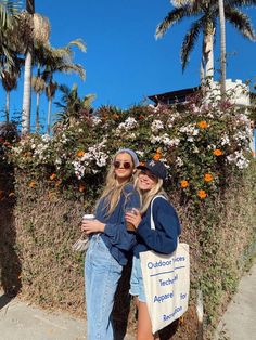 two women standing next to each other on the sidewalk with palm trees in the background