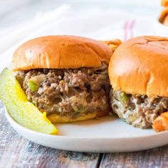 two pulled pork sandwiches with pickles on a white plate, ready to be eaten