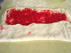 red and white cake sitting on top of a counter next to a person's hand