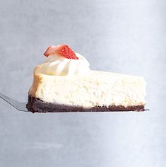 a piece of cheesecake is being held by a spoon with a strawberry on top