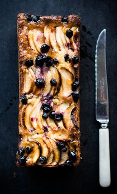 a piece of bread with blueberries and peaches on it next to a knife