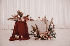 a table with flowers and candles on it next to a red cloth draped over the table