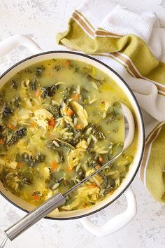 a white pot filled with chicken and spinach soup next to a green towel on top of a table