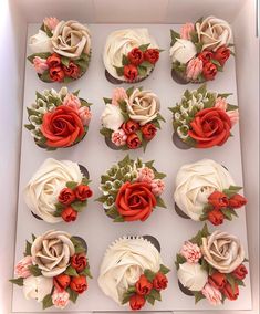 twelve cupcakes decorated with red and white flowers are in a box, ready to be eaten