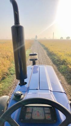 a tractor driving down a dirt road in the middle of a wheat field with sun shining on it