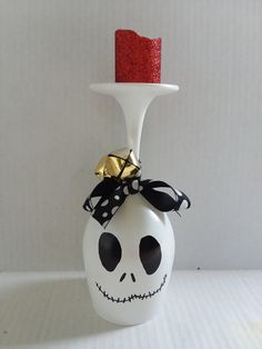 a white vase with a red candle in it and a skull decoration on the top