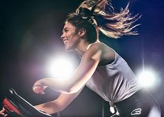 a woman on a stationary bike in front of spotlights with her hair blowing in the wind