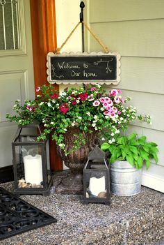 some flowers are sitting in buckets on the front porch with a sign above them