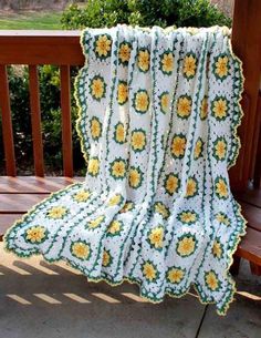 a white crocheted blanket with yellow flowers on it sitting on a wooden bench