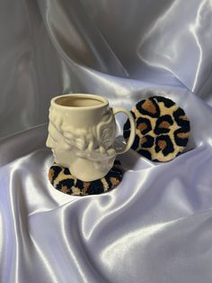 a cup and saucer sitting on top of a white cloth covered tablecloth next to a leopard print coaster