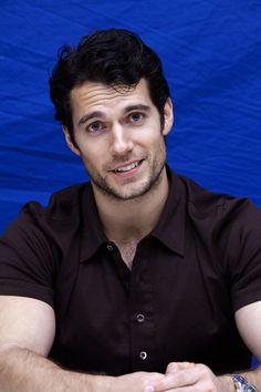 a man sitting in front of a blue backdrop with his hands folded on his chest