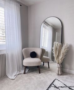 a chair sitting in front of a large mirror next to a tall vase filled with dry grass