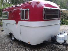 a red and white trailer parked on gravel next to trees