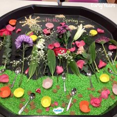 a tray filled with flowers and spoons on top of green grass covered in dirt