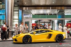 a yellow sports car is parked in front of a building with people standing around it