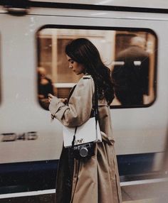 a woman standing in front of a train looking at her cell phone