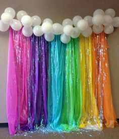 balloons and streamers are hanging from the ceiling in front of a rainbow colored wall