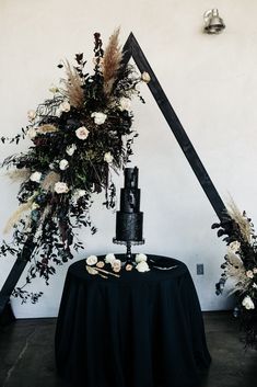 a black wedding cake with white flowers and feathers on the top is sitting on a round table