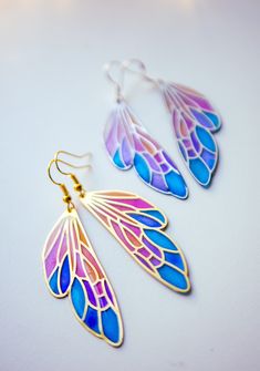 A beautiful fairy wing earrings inspired by stained glass compositions. Each of these butterfly wing earring holes are filled with different resin tones, creating a beautiful gradient aesthetic from blue to orange, which makes this pendant so magical and colourful. You can choose the necklace tone from two different tones, gold and silver. ✦ MEASUREMENT Wing: 50 X 17 mm ✦ DETAILS Wing pendant is made with gold or silver-plated brass. The earring hook is hypoallergenic. You can also choose Stainl Handmade Fairy Drop Earrings, Handmade Fairy Style Drop Earrings, Handmade Iridescent Jewelry In Butterfly Shape, Handmade Iridescent Butterfly Jewelry, Iridescent Butterfly-shaped Handmade Jewelry, Fairycore Butterfly Earrings For Gift, Handmade Winged Earrings For Gifts, Fantasy Earrings, Dragonfly Wings