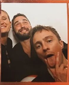 two men and a woman taking a selfie in front of a mirror with their tongue hanging out