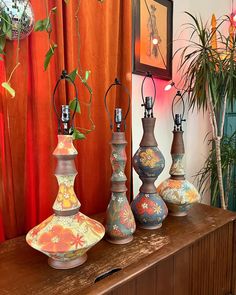 four vases are lined up on a table in front of an orange drapes