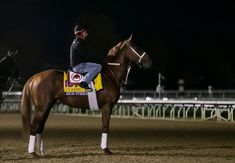 a man riding on the back of a brown horse in a race track at night