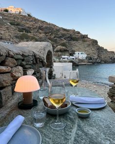 two glasses of wine are sitting on a table next to the water and some rocks