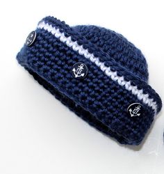 a crocheted blue hat with white stripes and anchors on the side is laying next to a pair of scissors