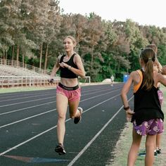 two girls running on a track with trees in the background