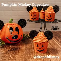 pumpkin mickey cupcakes with faces carved into them on a wooden table in front of a cake stand