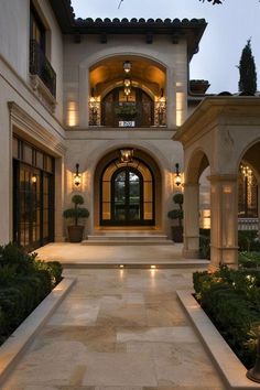 the entrance to a large home lit up at night with lights on and potted plants in front