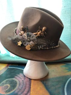 "Very unique soft brown felt fedora hat, \"Indiana Jones\" style by and hand decorated by Abracadebora in a \"Time is Precious so Hold on to your Hat\" theme. This is a one of a kind art creation and definitely a conversation piece. This soft brown fedora carries cupids, and hearts, a clock piece and feathers set into a vintage beaded brown ribbon band as a reminder that time is precious and cherished. Wearable art and unusual treasure." Custom Handmade Brown Top Hat, Custom Brown Brimmed Fedora, Handmade Vintage Mini Fedora, Handmade Brown Felt Hat For Western-themed Events, Handmade Brown Top Hat For Western-themed Events, Vintage Handmade Brown Hat Bands, Vintage Brown Handmade Hat Bands, Handmade Vintage Fedora Felt Hat, Whimsical Brown Hat With Curved Brim