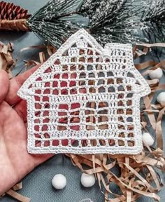 a hand holding a crocheted house ornament in front of christmas decorations