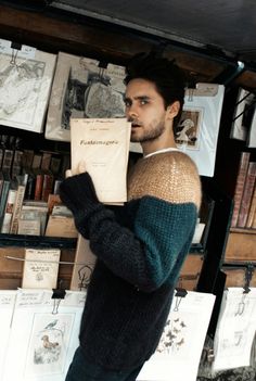 a man standing in front of a bookshelf holding a book